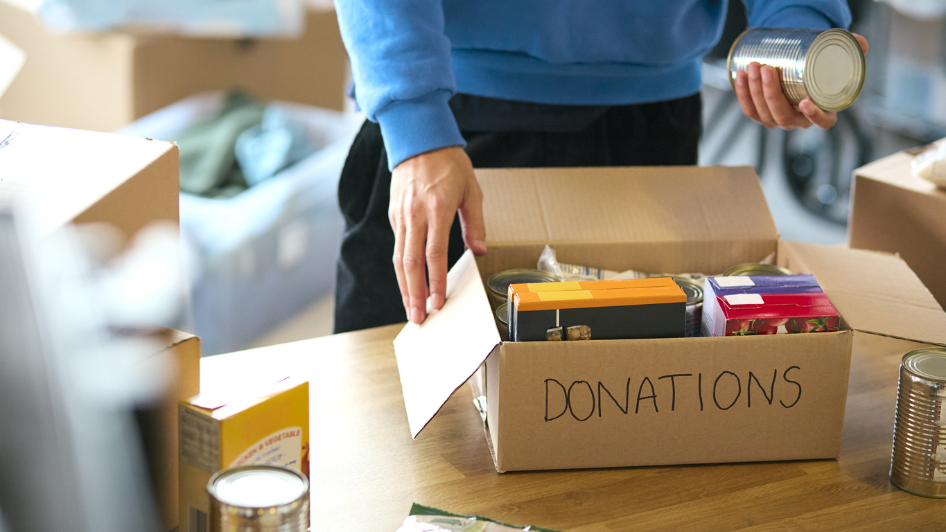 Canned food and oats packed into a cardboard box labelled donations.