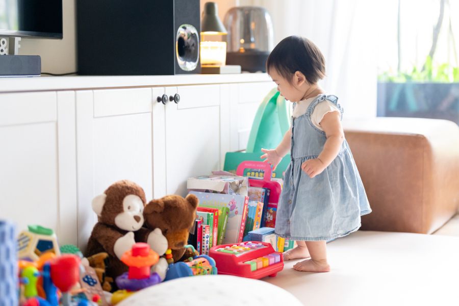 A toddler surrounded by toys in a living room, illustrating how quickly baby equipment takes over your home