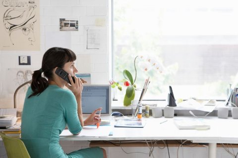 Woman sitting at a bright office desk working on a laptop and speaking on the phone, representing flexible office space to rent