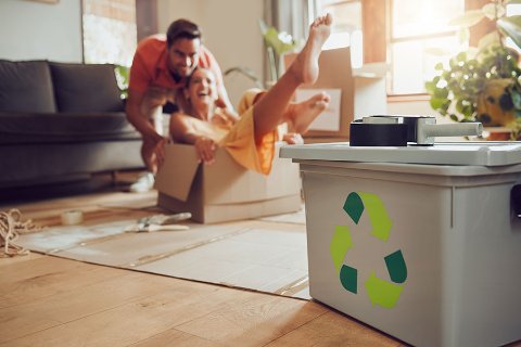 Couple playing in a moving box with a recycling symbol in the forefront of the image