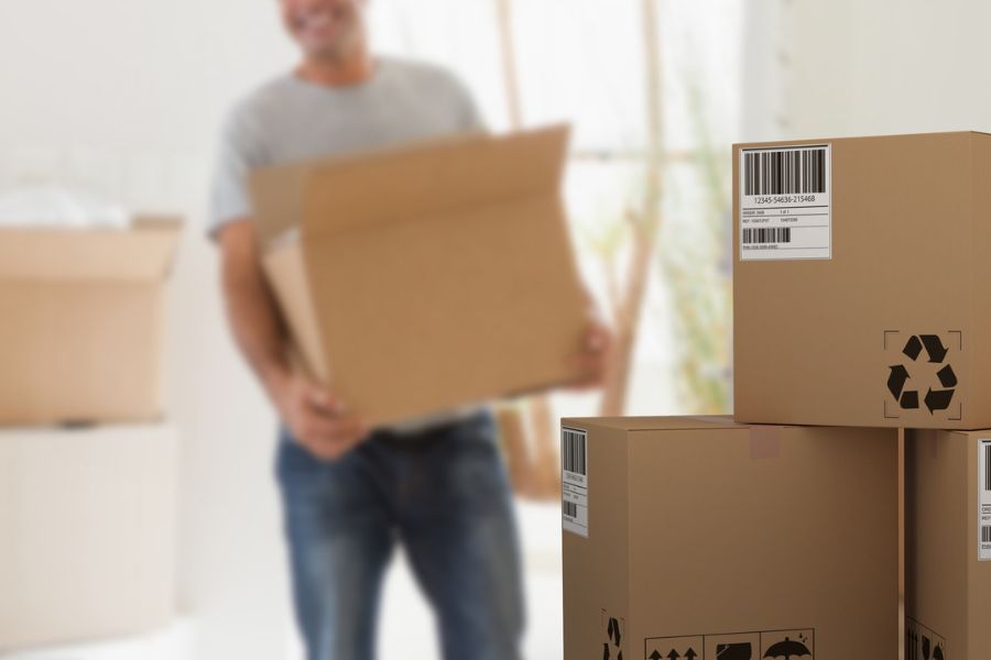 Man carrying a moving box with stacked cardboard boxes showing a recycle logo on moving day