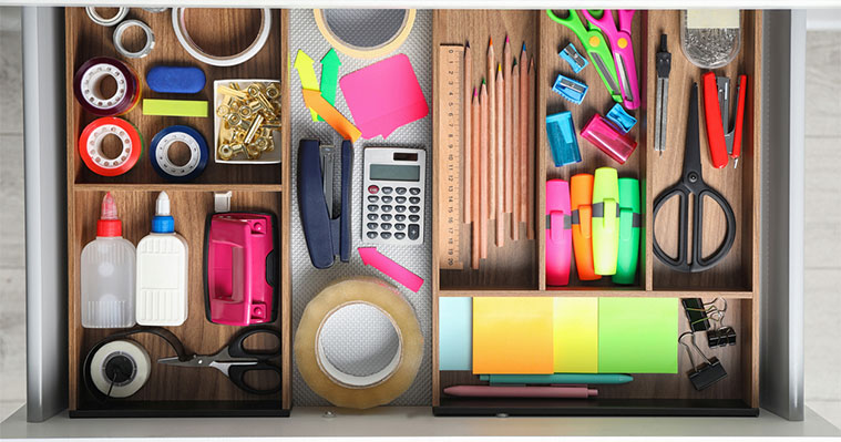 A drawer organiser filled with different office supplies (tape, calculator, ruler, pencil sharpeners)