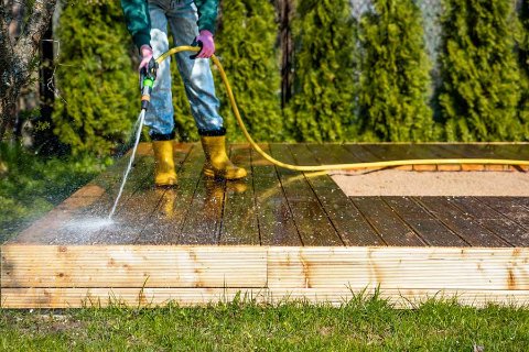 Person pressure washing a wooden deck in a garden, preparing it for spring or summer use.