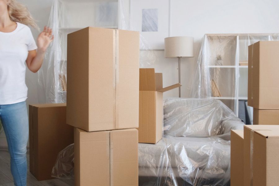Furniture covered in protective plastic and moving boxes in a room