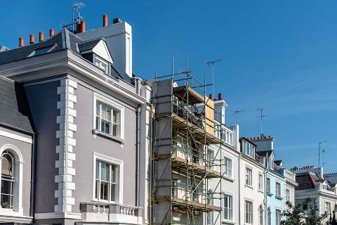 A row of colorful townhouses with scaffolding set up on one of the buildings under a clear blue sky.