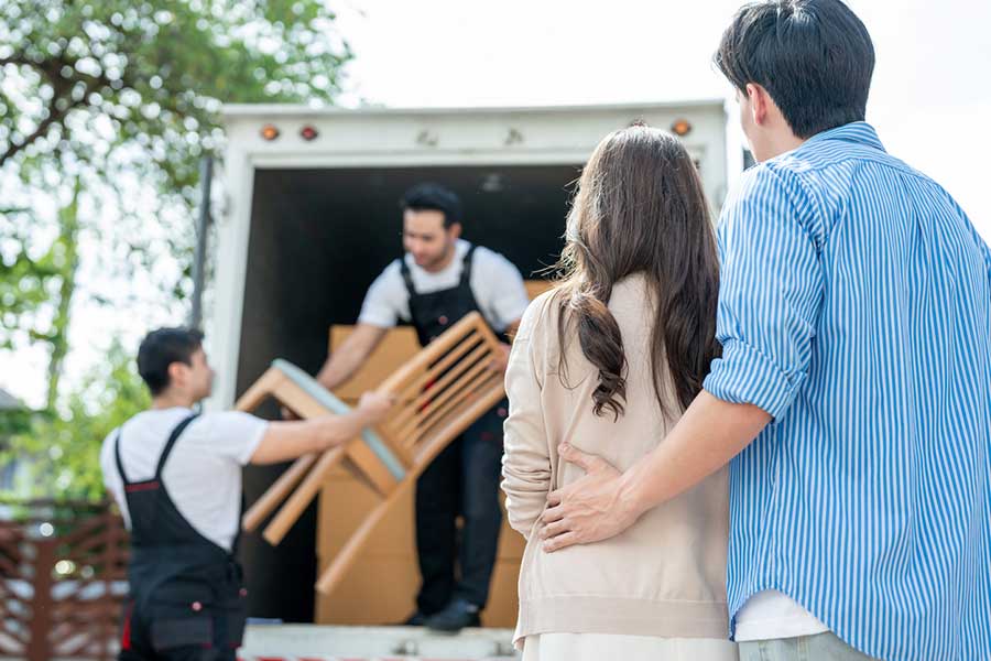 A couple watching charity workers load donated furniture, including chairs and boxes, into a van for collection.