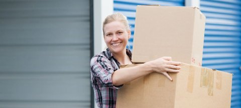 Woman carrying a cardboard box in front of an open self storage unit