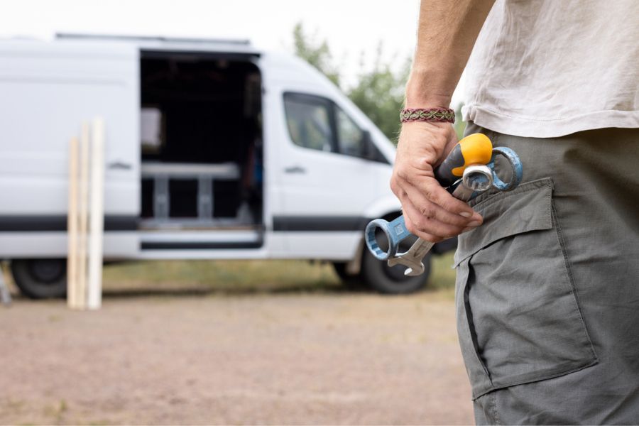 Tradesperson holding several tools beside a white van with wooden slats leaning against it
