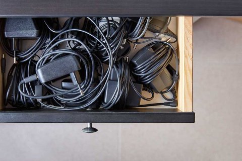 Drawer filled with tangled electrical cables and chargers, illustrating untidy wire storage.