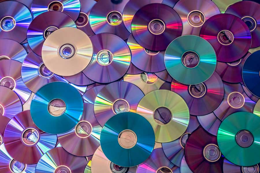 A colourful pile of old CDs and DVDs reflecting light, illustrating ways to repurpose or recycle outdated CDs and DVDs